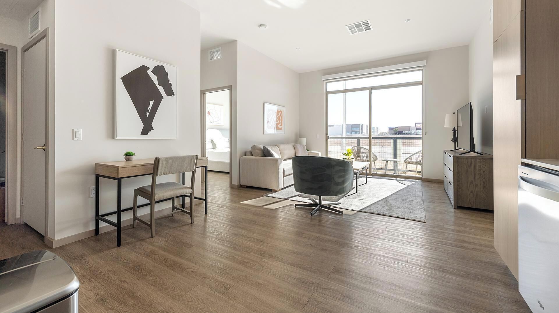 Una sala de estar moderna con piso de madera, un sofá gris, un sillón negro y un comedor con mesa y sillas.