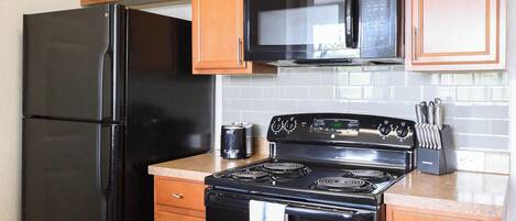 Una cocina con un refrigerador negro, un microondas, una estufa y armarios de madera.