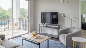 A modern living room with a TV, sofa, and a balcony with outdoor furniture. - Landing | Amazing 2BD, Pool, Clubhouse (Kissimmee)