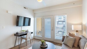 A modern living room with a flat-screen TV, a desk with a chair, a sofa, and a lamp. - Landing | Spectacular 1BD, Courtyard, Pool (Salt Lake City)