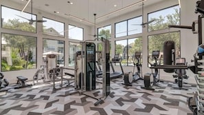 Un gimnasio con diverso equipo de ejercicio, amplias ventanas y un suelo estampado.