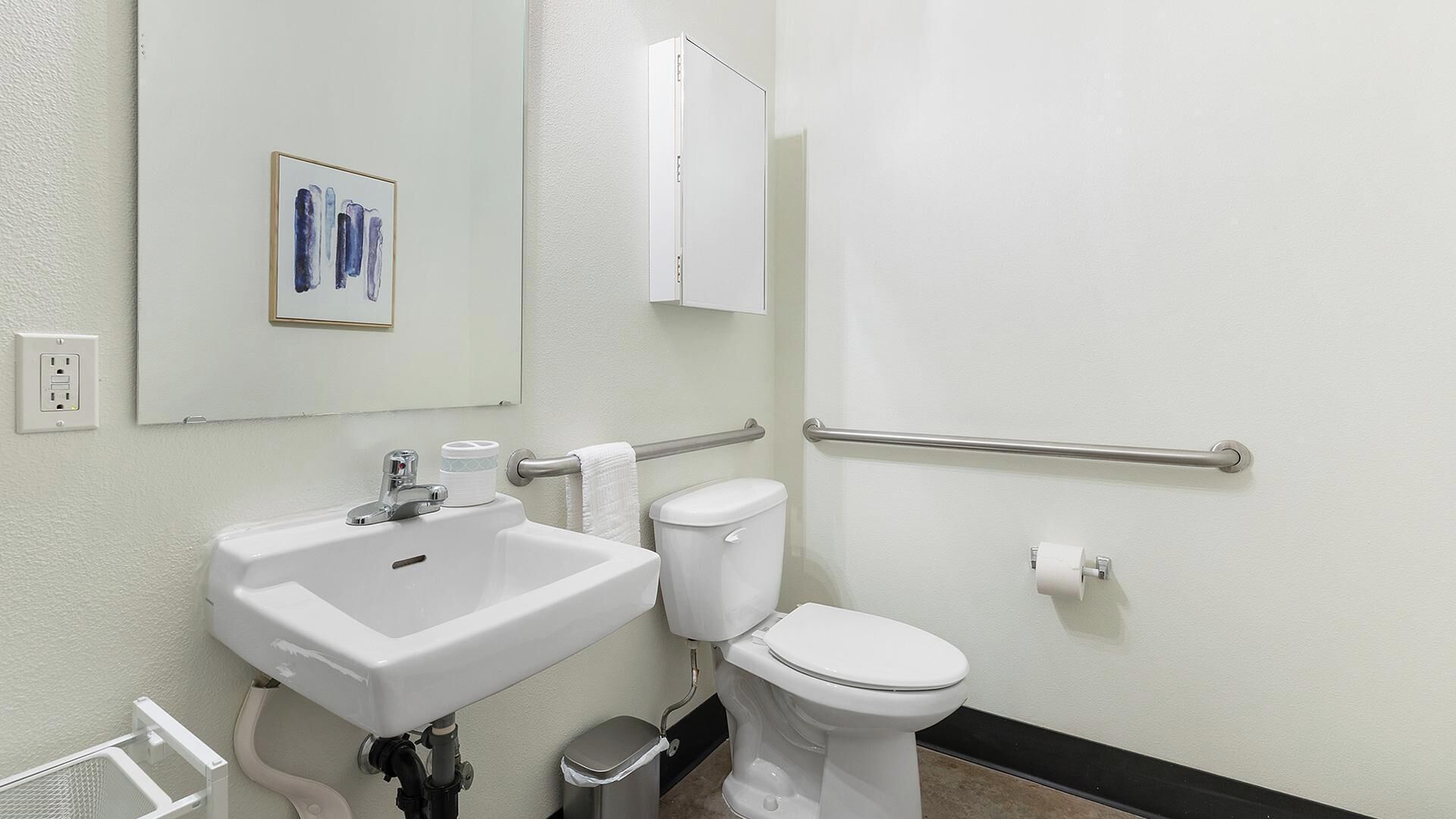 A bathroom with a white sink, toilet, and handrail.