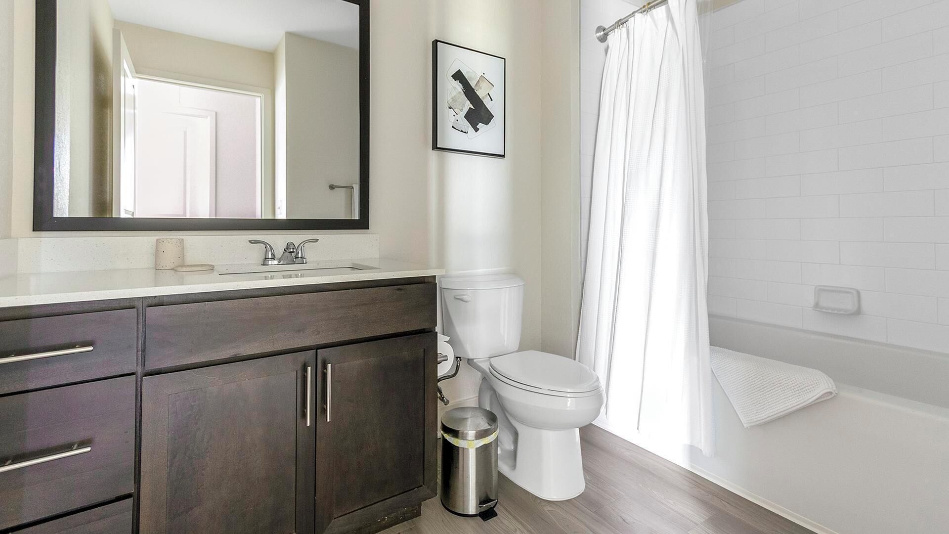 Une salle de bain avec un meuble-lavabo en bois foncé, des toilettes blanches et un rideau de douche.