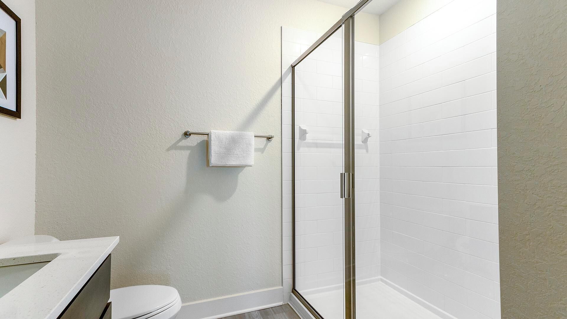 Un bagno con doccia rivestita di piastrelle bianche, un water e un lavandino.