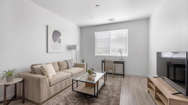 A modern living room with a sofa, coffee table, TV, and a desk with a lamp.