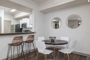A dining area with a round table, white chairs, and a woven chair. There are two round mirrors on the wall.