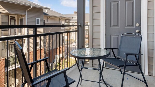 A balcony with a glass table and two chairs, overlooking a residential area.