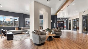 Een ruime, moderne lounge met een groot raam dat uitzicht biedt op de stad, een houten vloer en moderne zithoekopstellingen.