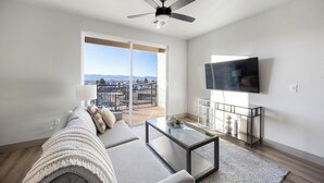 Een moderne woonkamer met een bank, salontafel en televisie. Het heeft een balkon met uitzicht op de stad.