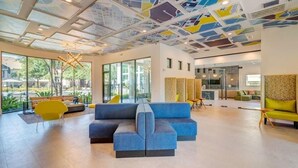 Een ruime lobby met een moderne blauwe hoekbank, gele stoelen en een plafond met een geometrisch patroon.