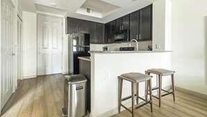 A modern kitchen with dark cabinets, stainless steel appliances, and a small island with bar stools.