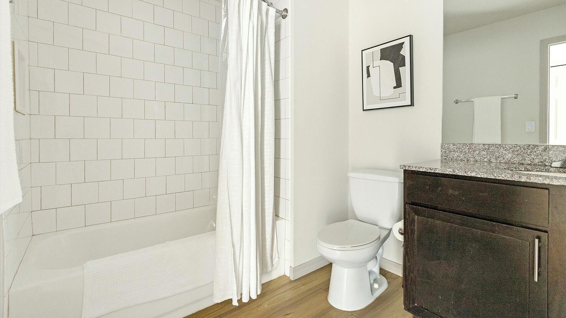 A bathroom with a white tiled shower, a white toilet, and dark wooden cabinets.