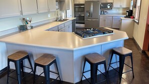 Una cocina moderna con armarios blancos, electrodomésticos de acero inoxidable y una isla central con taburetes.