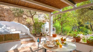 A covered outdoor dining area with a table set for two, surrounded by potted plants and a view of a rocky hillside. - La Cuadra in Frigiliana (Frigiliana)