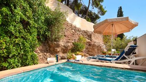 A swimming pool with lounge chairs and an umbrella, surrounded by greenery and a rocky hillside. - La Cuadra in Frigiliana (Frigiliana)