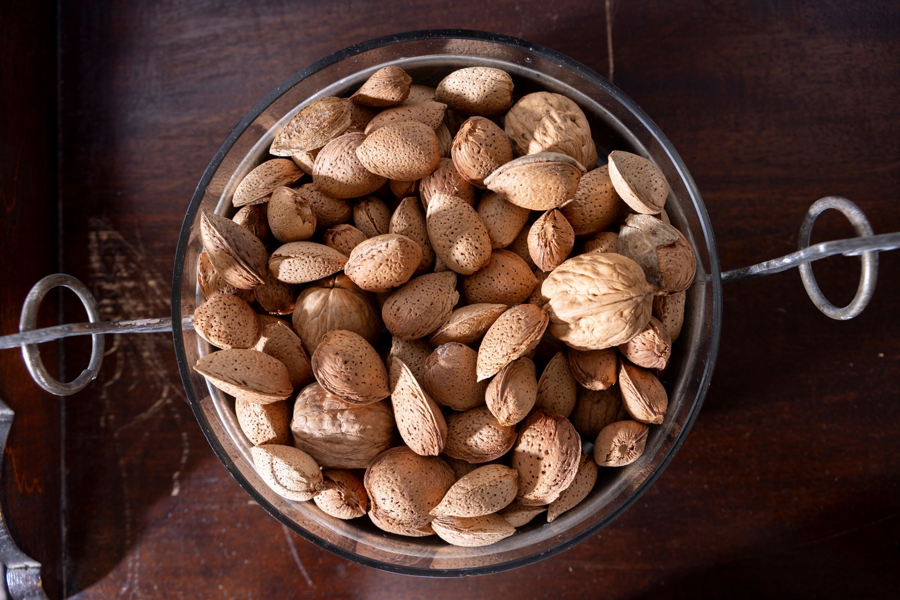 A clear glass bowl filled with almonds and walnuts on a wooden surface.