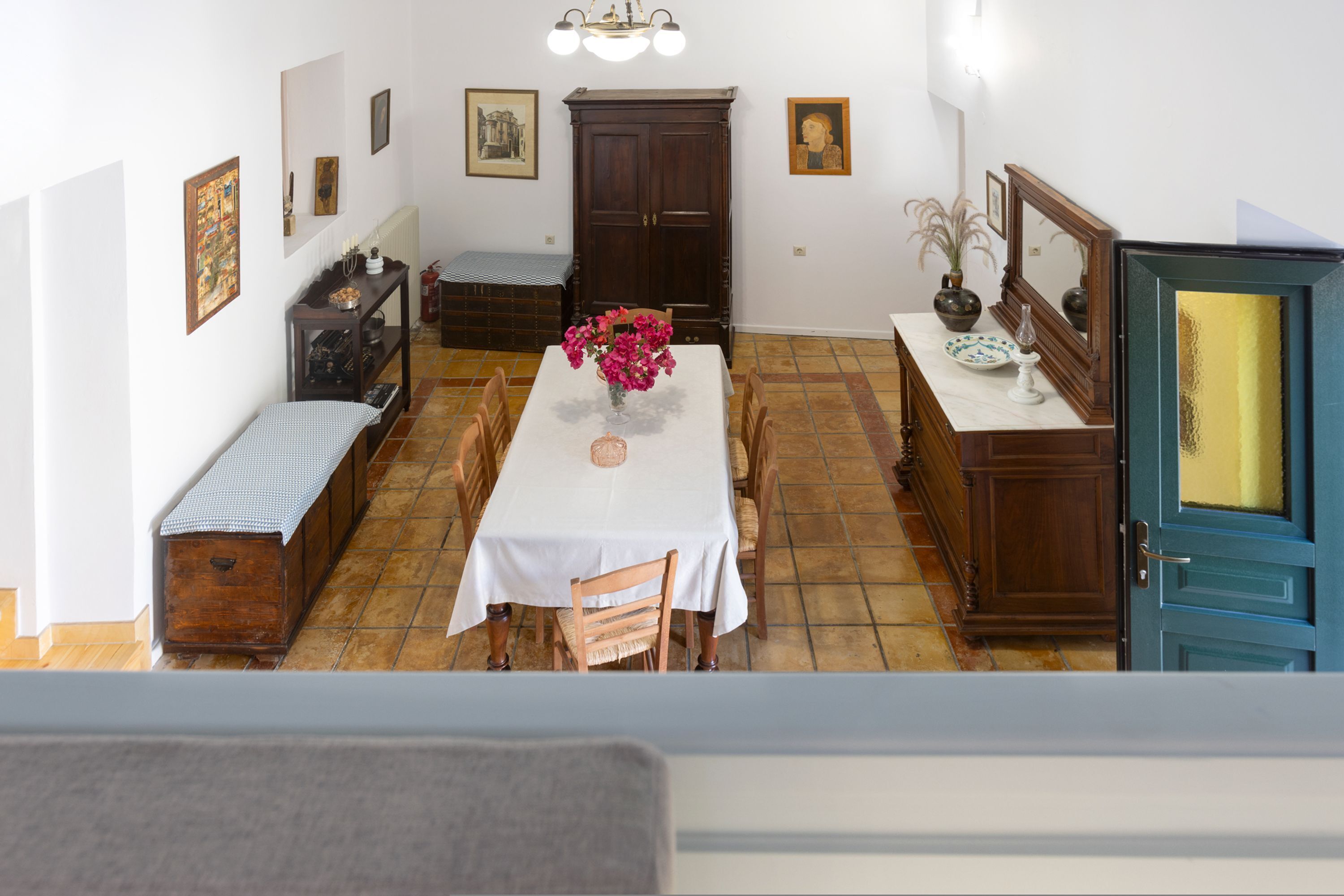 A dining area with a table set for four, surrounded by wooden chairs. A vase with flowers is on the table, and there are framed pictures on the walls.