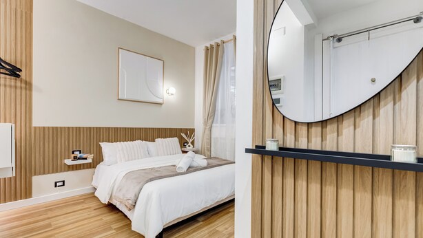 Een moderne slaapkamer met een bed, nachtkastje en een grote spiegel.