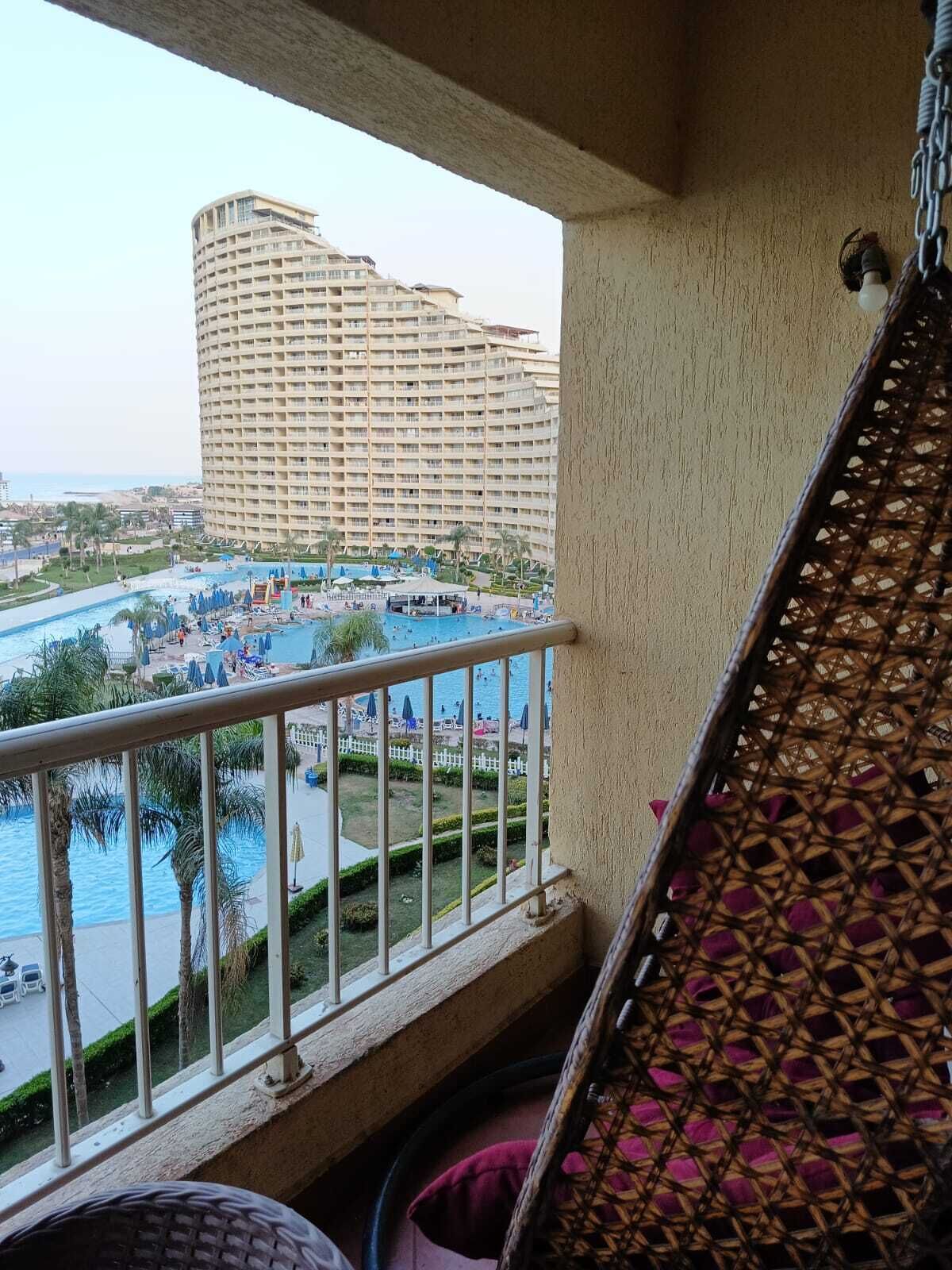 Un balcón con vistas a un hotel, una piscina y una playa.