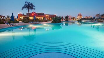 A swimming pool with lounge chairs and palm trees, surrounded by buildings with illuminated signs.