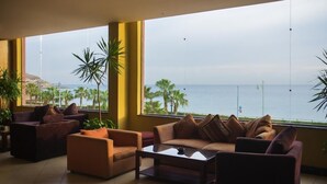 Amplia sala de estar con un gran ventanal que ofrece vistas al mar y palmeras.