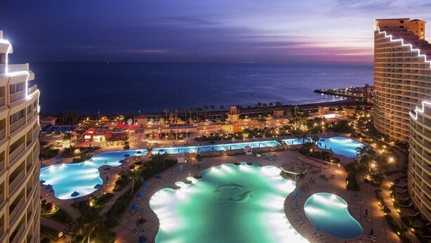 Un resort con varias piscinas, vistas a la playa y edificios iluminados.