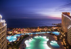 Ein Resort mit mehreren Schwimmbecken, Blick auf den Strand und beleuchteten Gebäuden.