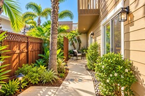 A residential outdoor space with a wooden fence, palm trees, a patio with chairs, and a pathway leading to a house. - Seaside Escape + Walk to Encinitas Beach + Wifi + Free Parking (Encinitas)