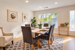 A dining area with a table set for six, surrounded by chairs, a sofa, and a small side table with a basket and vase. - Seaside Escape + Walk to Encinitas Beach + Wifi + Free Parking (Encinitas)