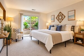 A bedroom with a large bed, a nightstand, a lamp, a chair, and a view of the outdoors. - Seaside Escape + Walk to Encinitas Beach + Wifi + Free Parking (Encinitas)