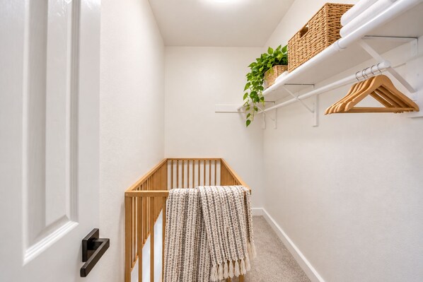 A narrow hallway with a wooden crib, a white door, and a shelf with baskets and a plant. - Seaside Escape + Walk to Encinitas Beach + Wifi + Free Parking (Encinitas)