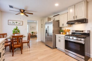 A modern kitchen with stainless steel appliances, wooden chairs, and a dining table. - Seaside Escape + Walk to Encinitas Beach + Wifi + Free Parking (Encinitas)