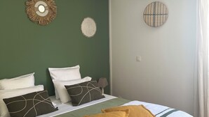 Siististi pedattu sänky, jossa on valkoiset ja vihreät vuodevaatteet, kaksi koristeellista seinävaatetta ja ikkuna, jossa on verhot.