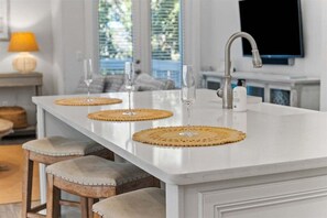 Eine Kücheninsel mit drei Barhocker, einem modernen Wasserhahn und einem flachbildfernseher, der darüber angebracht ist.