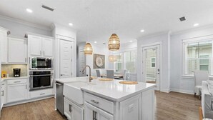 Une cuisine spacieuse avec des meubles blancs, un grand îlot central et des luminaires suspendus.
