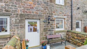 A stone building with two windows, a door, a bench, and a potted plant. - Clarence Cottage - UK47494 (Winkhill, near Leek)