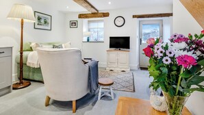 A living room with a sofa, a small table, a lamp, a TV, and a flower arrangement. - Clarence Cottage - UK47494 (Winkhill, near Leek)