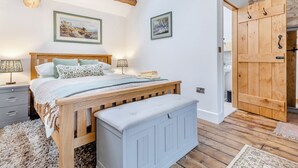 A bedroom with a wooden bed, a nightstand, a radiator, and a stone wall. - Clarence Cottage - UK47494 (Winkhill, near Leek)