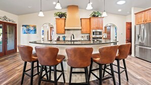 Una cucina moderna con isola centrale, sgabelli da bar, mobili in legno, elettrodomestici in acciaio inossidabile e luci a sospensione.
