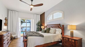 A bedroom with a bed, a dresser, a nightstand, a ceiling fan, a TV, and a window with blinds.