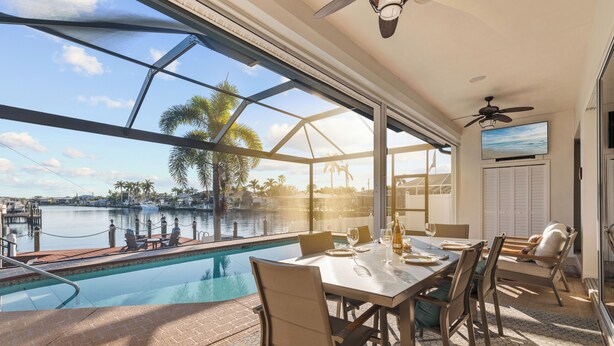 A dining area with a view of a lake, a pool, and palm trees.