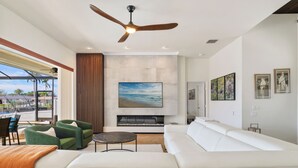 A modern living room with a white sofa, green armchairs, a fireplace, and a large painting of a beach scene.