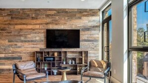 A modern living room with a stone wall, leather sofas, a coffee table, and a flat-screen TV.