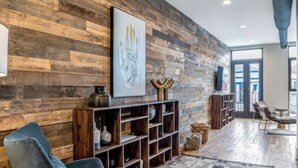 A modern living room with a wooden wall, a blue armchair, a patterned rug, and a bookshelf.