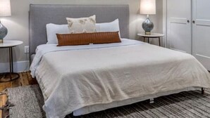 A modern bedroom with a large bed, two wall-mounted paintings, a ceiling fan, and a door to the right.