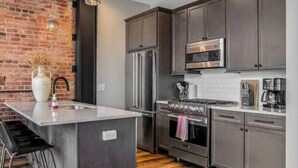 A modern kitchen with a central island, stainless steel appliances, and a brick accent wall.