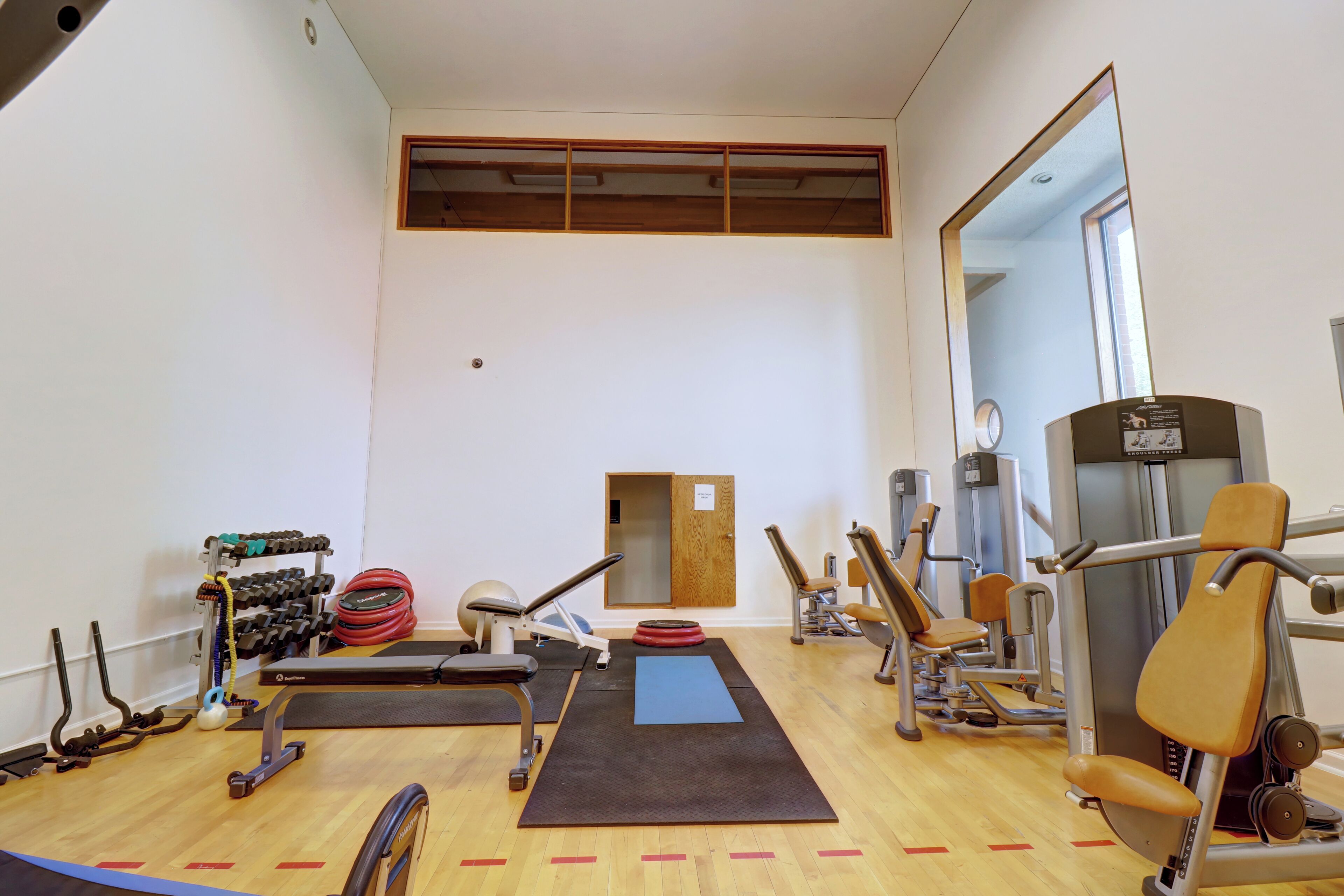 A gym with exercise equipment, a mirror, and a wooden floor.