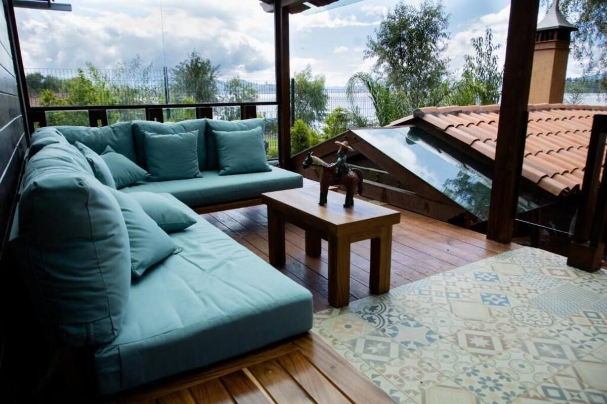 Uma área de estar externa aconchegante com um deck de madeira, um tapete estampado e vista para um lago.