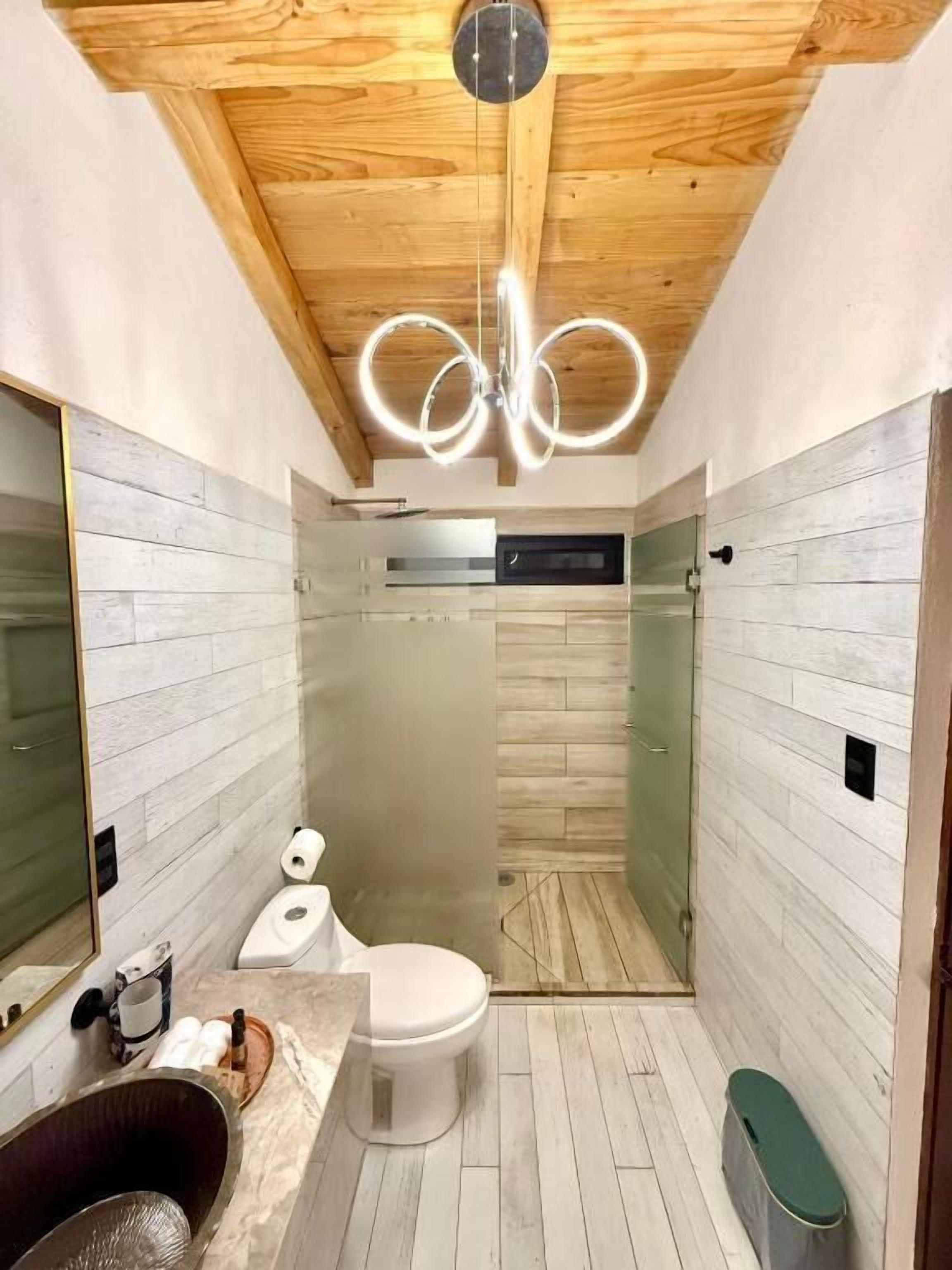 Ein modernes Badezimmer mit Holzboden, einer Duschkabine aus Glas, einer weißen Toilette und einer Marmorarbeitsplatte.