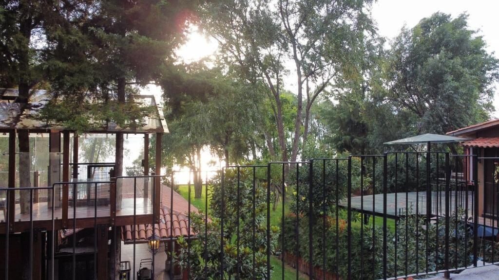A view of a property with a wooden deck, a fenced garden, and a building with a red roof.